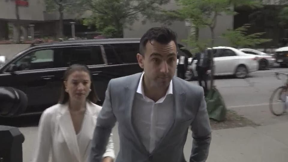 Accompanied by his wife, singer Jacob Hoggard enters the Toronto courthouse, wearing a light gray suit and a white shirt.