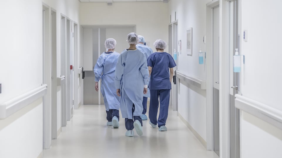 Four medical workers walk with their backs down a hospital corridor.