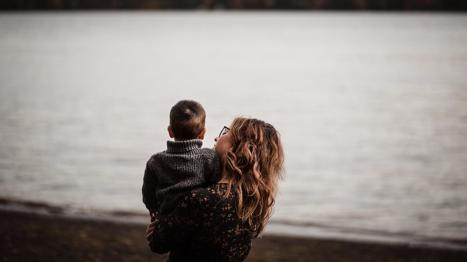 A mother holds her son in her arms in front of a lake.