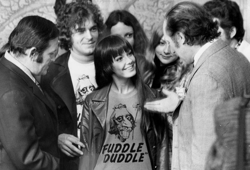 Then Prime Minister Pierre Trudeau smilingly points at his caricature on a "fuddle duddle" shirt worn by Nada Simard, 16, visiting Parliament Hill after winning a radio station contest.  The shirts were rushed into stores when Trudeau denied he'd mouthed an obscenity in the House.