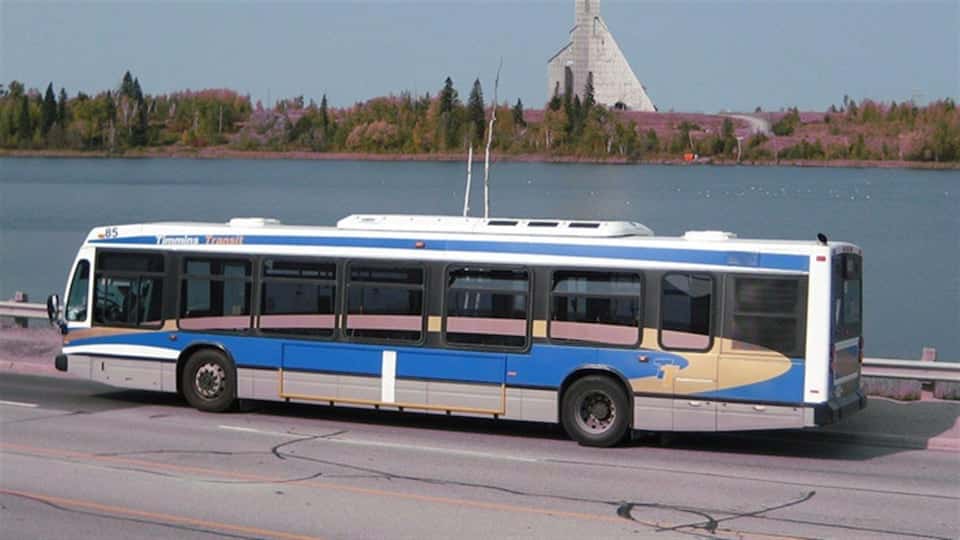 A bus driving in front of a lake in Timmins.
