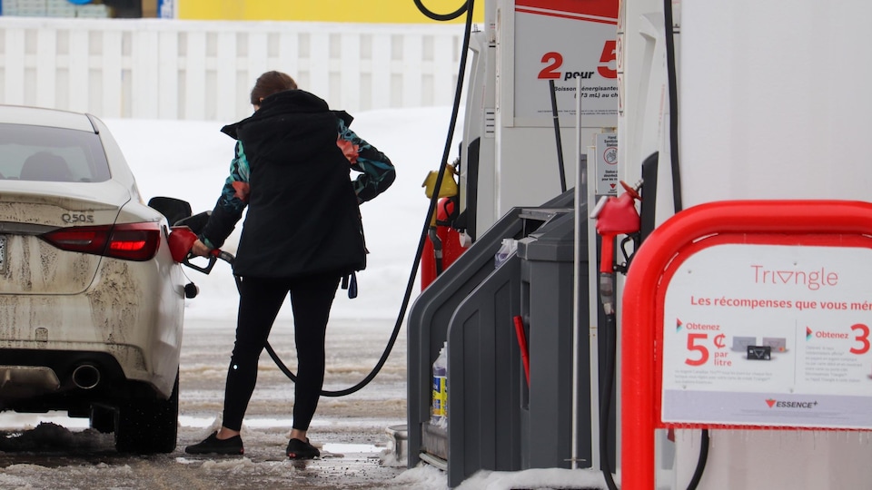 A woman from behind at a gas station filling up her car.  There is snow on the ground.