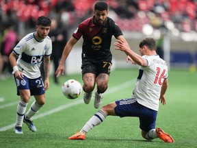 Valor FC's Federico Pena (77) jumps to avoid the tackle by Vancouver Whitecaps' Sebastian Berhalter (16) as Ryan Raposo (27) watches during the first half of a preliminary round Canadian Championship soccer match, in Vancouver, on Wednesday, May 11, 2022.