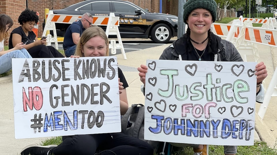 Two women hold signs in English: one reads 'Abuse has no gender #MenToo', and the other, 'Justice for Johnny Depp'.