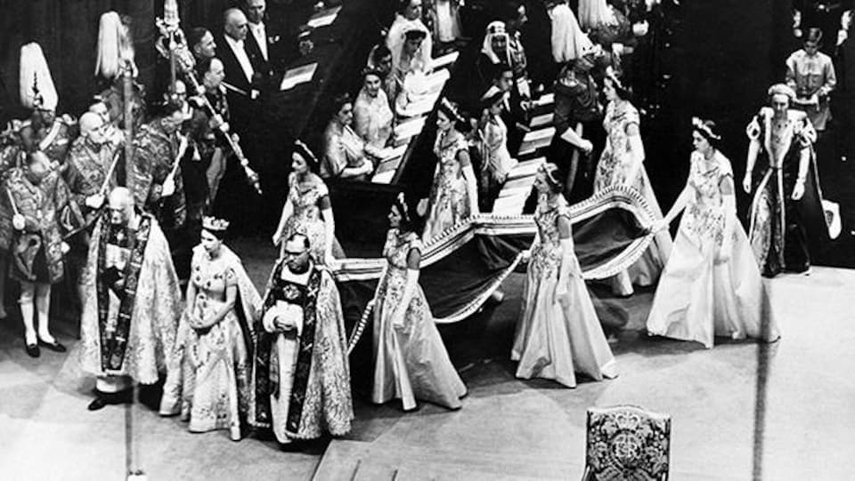 Queen Elizabeth II followed by six women holding the train of her dress during her coronation at Westminster Abbey.