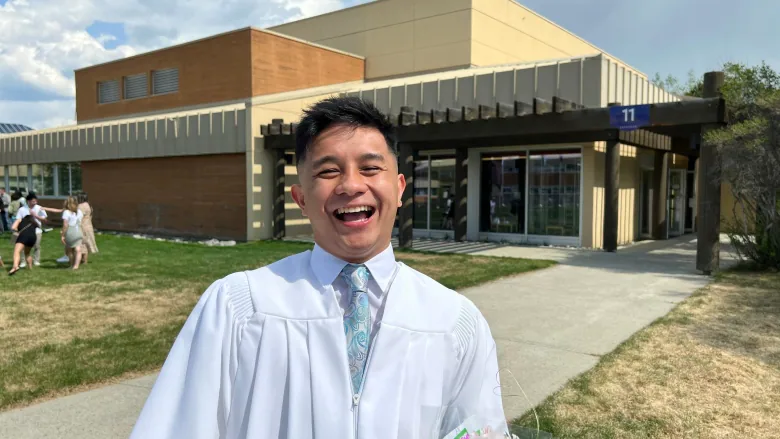 Floyd Guanga smiles big while wearing a white robe at his graduation