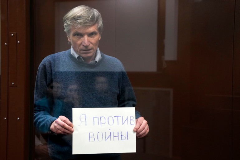 Alexei Gorinov holds a sign saying "I am against the war" while standing in a courtroom enclosure.
