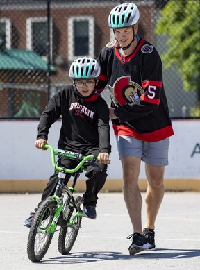 Ottawa Senators defenseman Nick Holden helps 9 year old Abdil Bari learn to ride a bike after bike helmets were given to neighborhood kids.
