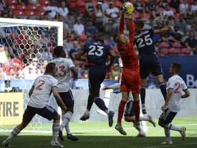 Vancouver Whitecaps goaltender Cody Cropper (55) jumps to grab the ball between New England Revolution defender Jon Bell (23) and midfielder Brandon Bye (15) during the first half at BC Place.