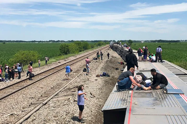 A train lying on its side after derailing with people on top helping the injured.