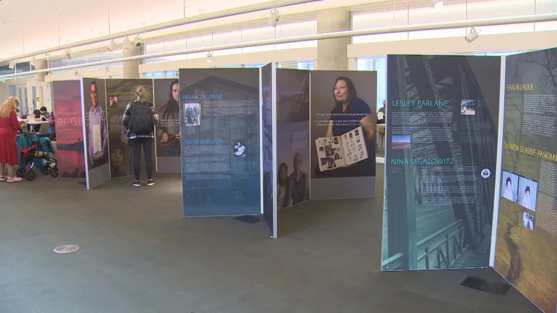 An exhibit display that has multiple panels with the photos and stories of Sixties Scoop survivors.