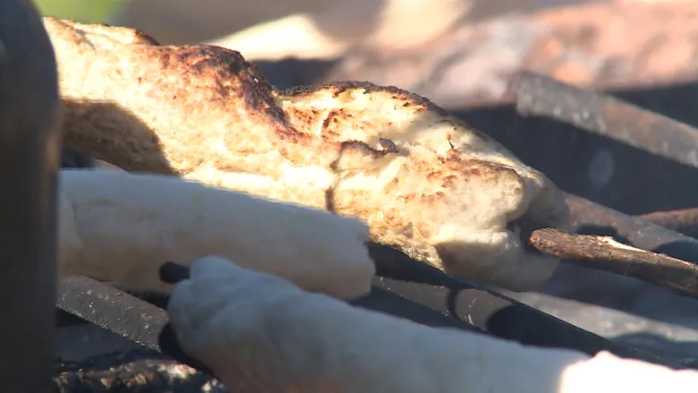 Bannock is cooked outdoors on a stick, over an open flame.