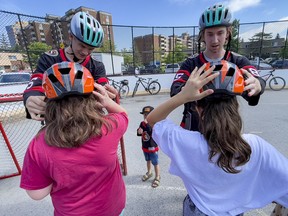 Senators players Nick Holden, left, and Jake Sanderson help fit kids from Bayshore Public School with new bike helmets on Friday.