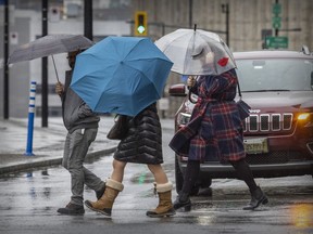 Pedestrians shelter under umbrellas while crossing Peel St. on a rainy day in Montreal.  Expect more of the same overnight Wednesday into Thursday.