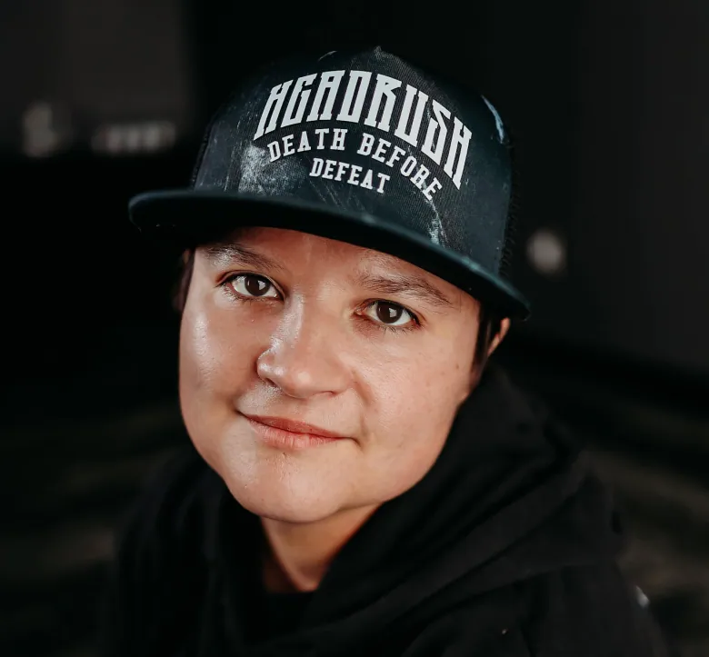 A person looks up into the camera wearing a black ballcap reading 'Headrush' and 'death before defeat,' and a black hoodie.
