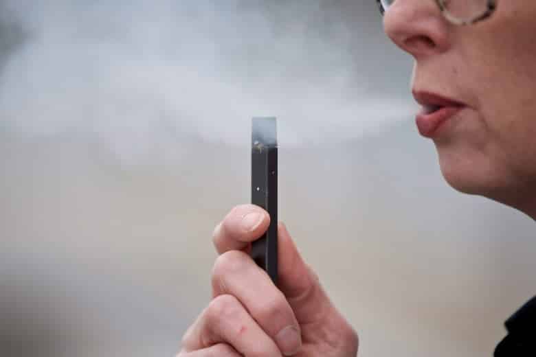 A woman holds an electronic cigarette device and exhales a puff of steam.